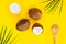 Top view organic bio coconut butter with two whole fresh coconuts, one half and palm leaves on yellow background