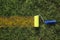 Top view of a paint roller with an blue handle, painting a grassy strip using orange color. Autumn. Ecological concept