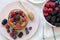 Top view, pancakes with berries and honey on a pink plate, bowl of berries. Closeup. Flat lay