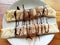 Top view of pancakes rolled into a tube lying on a plate and poured with chocolate