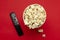 Top view of paper bucket full of sweet popcorn and black clicker on the red surface