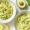 Top view on pasta with avocado and Greek basil sauce in a ceramic bowls on a white table