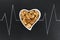 Top view of peeled walnuts in heart shaped bowl on black slate plate with chalk drawn heartbeat cardiogram