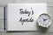 Top view of pencil,clock and notebook written with Today`s Agenda on white wooden background