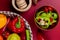 top view of pepper slices in bowl with vegetables as pepper tomato in basket with garlic crusher on bordo background