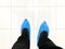 Top view of person`s feet shoes wearing medical antibacterial blue plastic disposable pull on slippers covers in hospital
