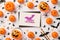 Top view photo of black envelope glitter purple bat inscription happy halloween on white card pumpkin baskets candy corn straws