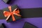 Top view photo of black giftbox with orange ribbon bow boxes on isolated violet and black background with copyspace
