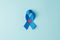 Top view photo of blue ribbon and small red heart symbol of prostate cancer awareness on isolated pastel blue background