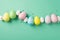 Top view photo of easter decorations glowing confetti and row of multicolored easter eggs on isolated teal background with