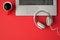 Top view photo of grey laptop red cup of drink and white bright headphones on isolated red background with copyspace