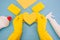 Top view photo of hands in yellow rubber gloves holding yellow paper heart, multicolored sponges, rayon rags, bottles of detergent