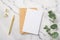 Top view photo of paper sheet craft paper envelope gold pen binder clips and eucalyptus branch on white marble background with