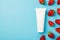 Top view photo of scattered strawberries water drops and white cream tube on isolated light blue background with copyspace on the