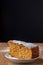 Top view of piece of carrot sponge cake with icing sugar on plate on wooden table and black background