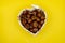 Top view of a pile of hazelnuts in a heart shaped container on the yellow surface