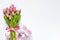Top view of pink tulips bouquet, wrapped with pink ribbon and pink dotted gift box over white background. Copy space.