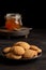 Top view of plate with cookies, spoon and jar of jam on dark table, selective focus, black background,