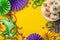 Top view of a plate filled with tempting cupcakes, an opulent masquerade mask, vibrant beads, feather on yellow backdrop