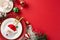 Top view plates, charming gold cutlery in pocket, napkin, mug, candy cane, ornaments, frosted fir twigs on red backdrop