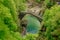 Top view on the Ponte Romano Intragna Bridge hiding in the valley with beautiful river covered with trees, close to