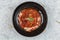 Top view of Pork rib chops steaks boiled with tomato sauce and cheese served in black round plate on washi Japanese paper