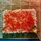 Top view of process of spreading red caviar over cooked rice on seaweed wrap while making delicious rolls