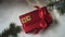 Top view of a red box with a bow lies on the snow under the Christmas tree. A woman\'s hand lays out the word SALE