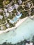 Top view of a resort with nipa roofed bungalows and a swimming pool with a beachfront with white sand and shallow sloping coast.