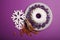 Top view of ring cake with an alight candle, cinnamon, almond and white snowflakes on a bright violet background.