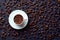 Top view of roasted whole coffee beans in white porcelain cup on saucer on gray background