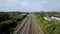 Top view of rows of long railways layng along green line of bushes and trees