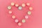 Top view of rows of unused multicolored wax tea light candles laid out in the shape of a heart on pink background.