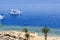 Top view of a sandy beach with sunbeds and sun umbrellas and two large white ships, a boat, a cruise liner floating in the sea on