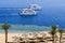 Top view of a sandy beach with sunbeds and sun umbrellas and two large white ships, a boat, a cruise liner floating in the sea on