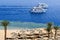 Top view of a sandy beach with sunbeds and sun umbrellas and two large white ships, a boat, a cruise liner floating in the sea on