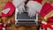 Top view Santa hands in white gloves are typing on keyboard laptop by wooden New Year decorated table. Santa Claus looks