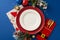 Top view of Santa\\\'s coat-shaped holder for gold cutlery, plated, napkin, candle and festive adornments on blue background