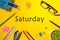 Top View of Saturday - word on yellow workplace with office or school supplies. Time Management and Schedule Concept