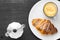 Top view on a served italian breakfast with cappuccino, moka and croissant on a black background.