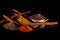 Top view of several ground spices, cinnamon twigs, and peppercorns in a white bowl on a black table. Concept of gastronomic