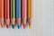 Top view of several ordered colored pencils on white wooden background