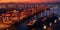 Top view of shipyard at dusk, with colossal cranes silhouetted against setting sun, lifting containers onto massive