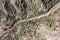 Top view shot of a narrow road through the brown rocky hills covered with green plants