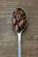 Top view of a silver teaspoon filled with roasted coffee beans on a wooden table.