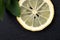 Top view of sliced yellow lemon with leaves of fresh lemon balm on black background