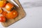 Top view of slices of persimmon and whole one, knife on the wooden cutting board, white kitchen table