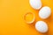 Top view of smashed chicken egg with yolk on bright orange background among white whole eggs.