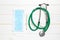 Top view of stethoscope, protective mask and mercury thermometer on white wooden background. Medical instruments concept