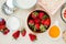 top view of strawberries in bowl and glass of milk and melted butter with flour and oats on white background